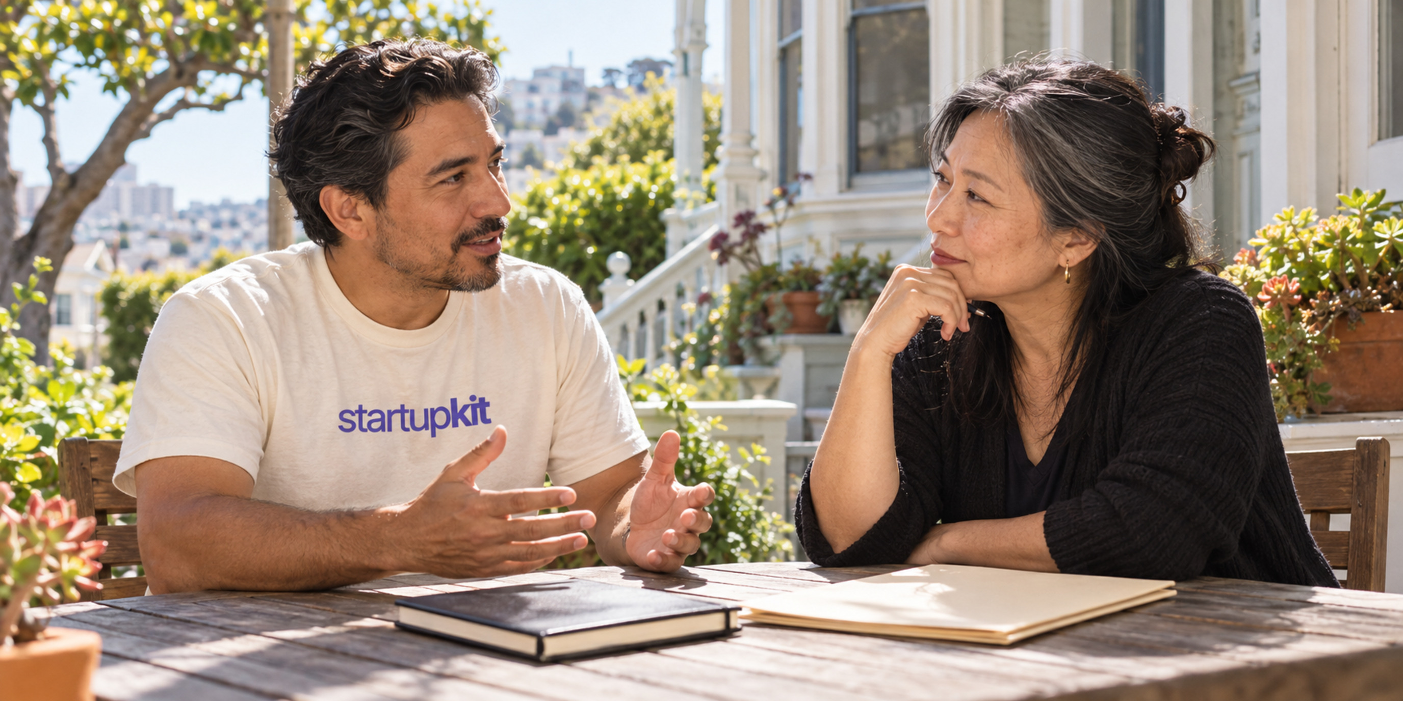 A founder and finance lead discussing a hiring request at an outdoor table with a closed notebook