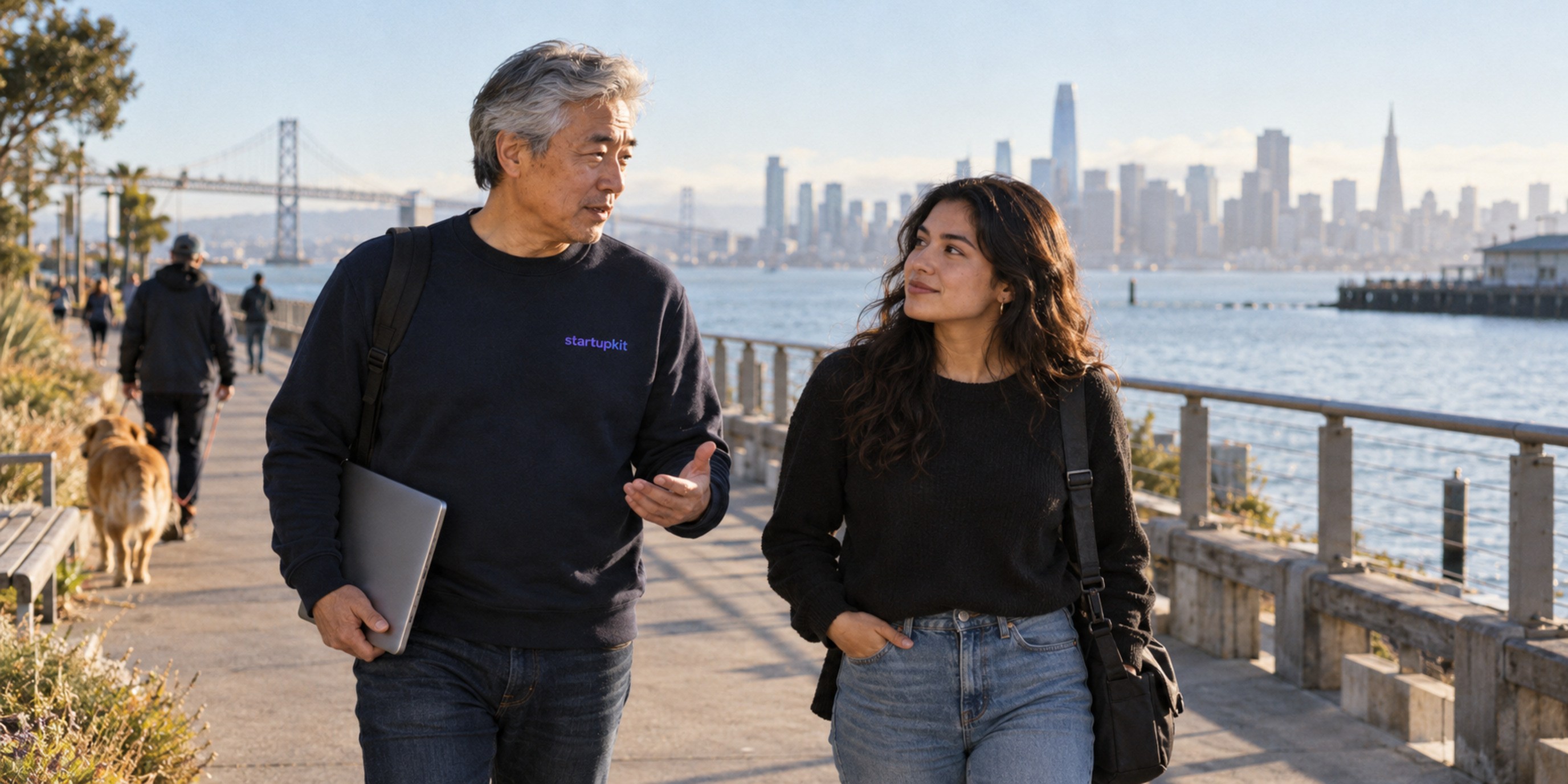 An older East Asian male mentor and a younger Latina engineer talk during a walk along the San Francisco waterfront.