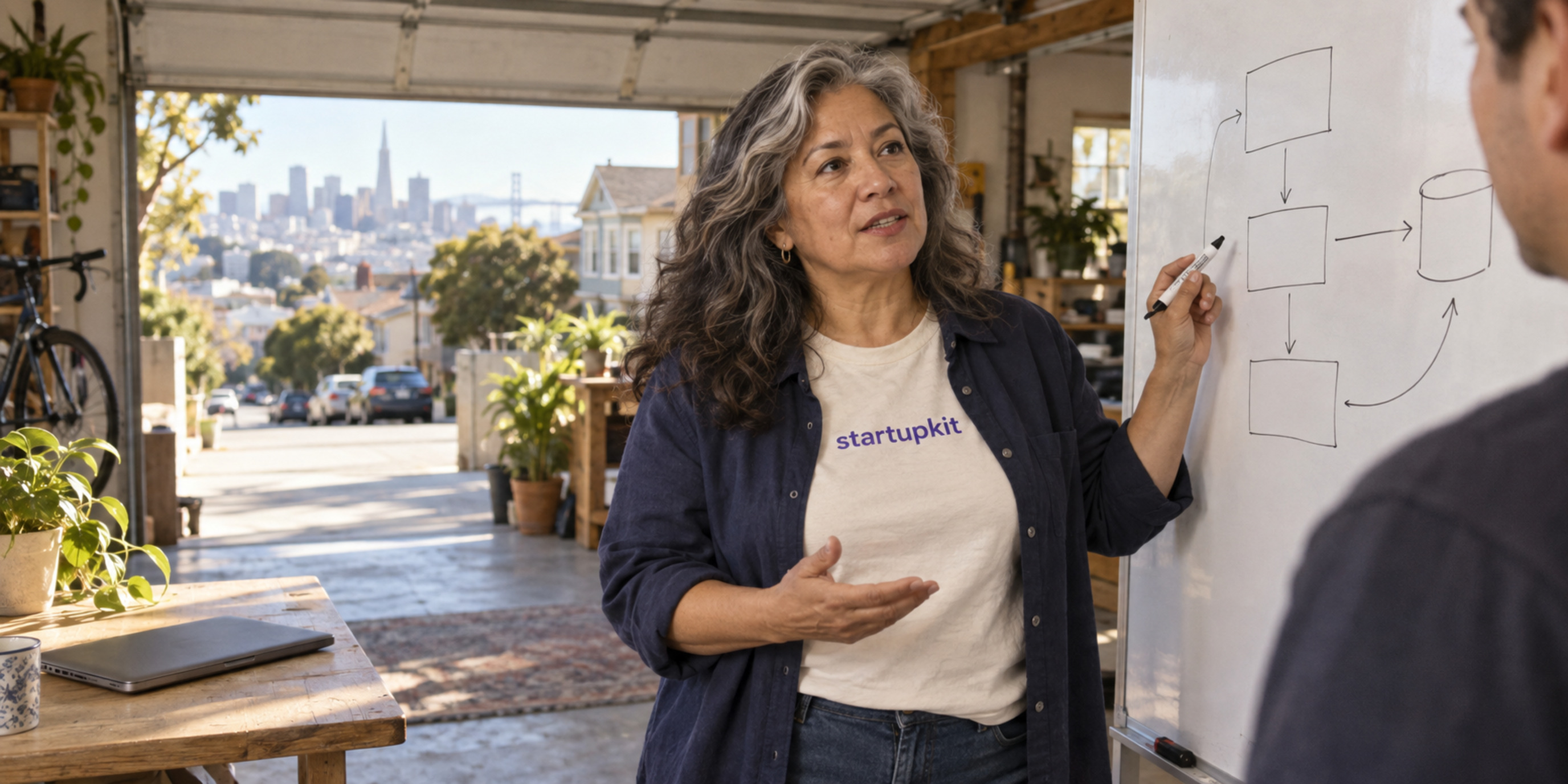 A Latina engineer in her 50s discusses a simple system sketch in a sunlit San Francisco garage workspace