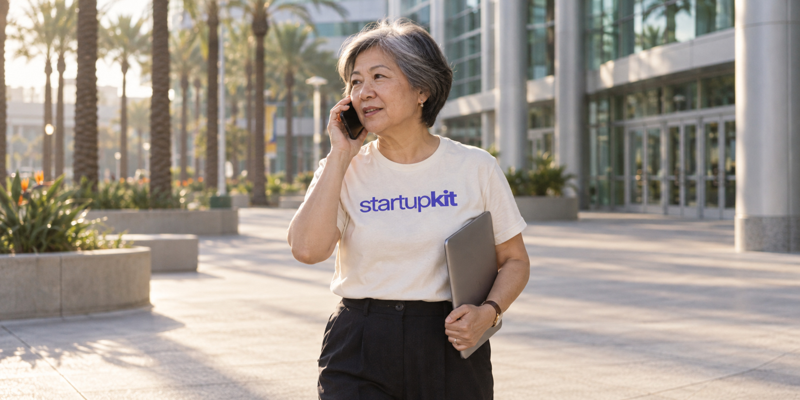 Recruiter speaking by phone outside a conference center while holding a closed laptop